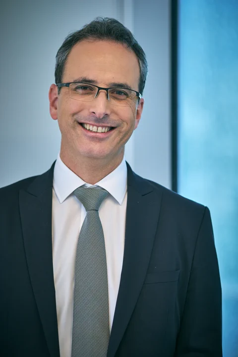 צילום תדמית של איש עסקים בחליפה כהה על רקע חלון משרד מואר — צילום תדמית עסקית תל אביב