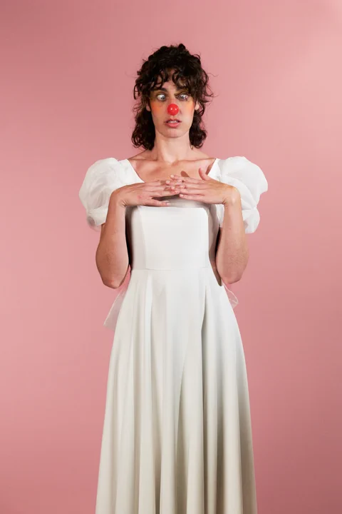 צילום קונספטואלי של דמות עם אף ליצן אדום ושמלה לבנה על רקע ורוד — אולפן צילום סטילס תל אביב